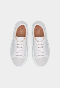 Ζευγάρι λευκά δερμάτινα sneakers με κορδόνια, διακοσμημένα με διάτρητες λεπτομέρειες και ταμπά εσωτερικά πέλματα με την επιγραφή "AGL", εμφανιζόμενα από πάνω σε λευκό φόντο.