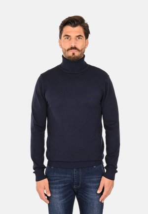 Maglione a collo alto di colore blu navy realizzato in tessuto a maglia liscia, con un design aderente e polsini e orlo a costine, indossato con jeans scuri.