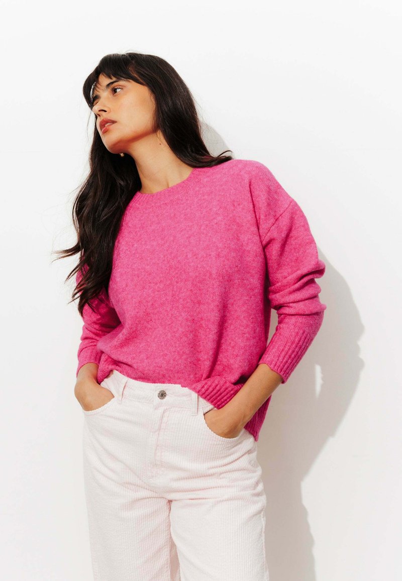 Pull en tricot fuchsia avec des poignets et un ourlet côtelés, associé à un pantalon en velours côtelé rose clair avec des poches latérales et une fermeture à bouton.