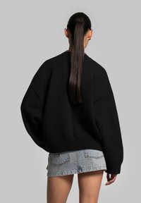 Black oversized knit sweater with ribbed texture, paired with light blue denim shorts. The sweater features dropped shoulders and a wide fit.