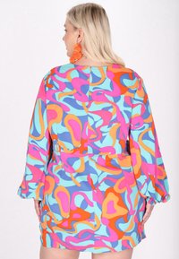 Rochie colorată cu modele abstracte vibrante în nuanțe de roz, albastru, portocaliu și galben, cu mâneci lungi și croială lejeră.