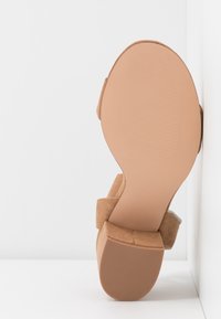Sandale en daim marron avec talon bloc, semelle face à l'avant sur un fond blanc en angle.