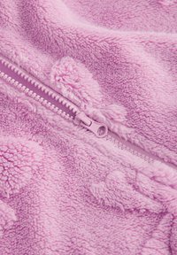 Tissu en polaire rose présentant une surface texturée avec un détail de fermeture éclair. Sensation douce et moelleuse avec un motif légèrement en relief sur l'ensemble.