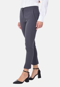 Pantaloni grigi su misura con vita alta e tasche laterali, abbinati a scarpe nere con tacco alto dotate di cinturini alla caviglia.