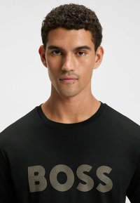 Black t-shirt featuring a prominent gold "BOSS" graphic. Crew neckline, short sleeves, cotton material with smooth texture.