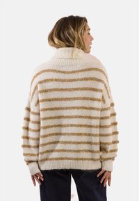 Maglione beige oversize con strisce orizzontali dorate. Presenta un collo alto e polsini a costine, realizzato in un morbido tessuto a maglia testurizzato.