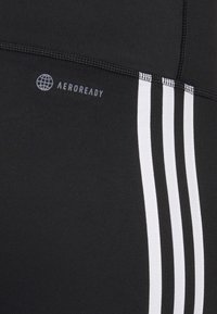 Czarne legginsy sportowe z trzema białymi paskami po jednej stronie, charakteryzujące się gładką teksturą i logo z napisem "AEROREADY".