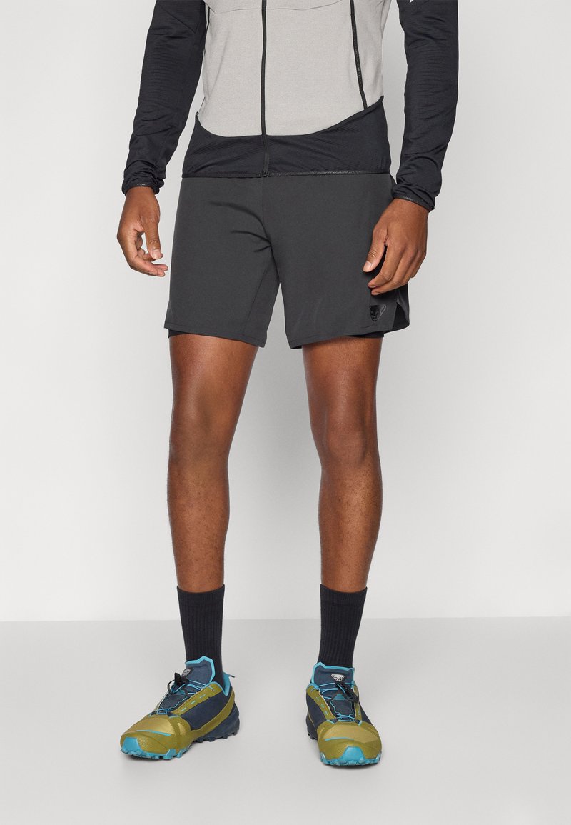 Shorts de sport noirs pour homme avec des poches, associés à un haut à manches longues gris et noir, et des chaussures de trail robustes turquoise et vert.