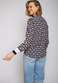 Marinebluse mit weißen, runden Mustern, langen Ärmeln und gestreiften Bündchen. Kombiniert mit hellblauen, weit geschnittenen Jeans.