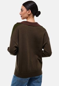 Pull en cachemire marron surdimensionné avec un col marron et des accents verts sur les épaules. Texture douce, dos plus long et ourlet côtelé. Style décontracté avec une coupe ample.