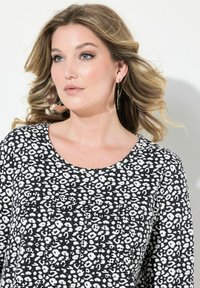 Zwart-wit gevlekte top met lange mouwen en een ronde halslijn. Beschikt over een zachte stoftextuur en subtiele versieringen aan de voorkant.