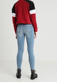 Punainen ja musta väri-blockattu villapaita, jossa on valkoisia raitoja, yhdistettynä sinisiin slim fit -farkkuihin ja mustiin nilkkabootseihin, joissa on kiiltäviä yksityiskohtia.