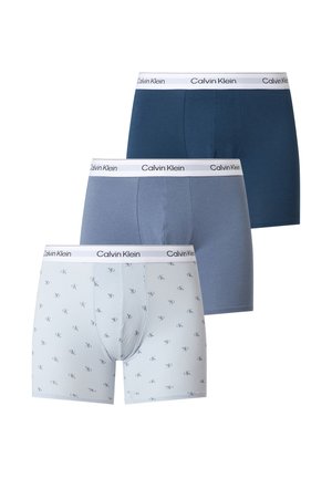 Trois paires de boxers Calvin Klein en blanc avec logos, bleu clair et bleu foncé, chacun avec une ceinture blanche marquée Calvin Klein.