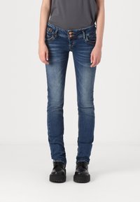 Smala blå jeans med en blekt tvätt, två framfickor och dubbelknäppning, matchade med svarta skor. Slät denimtextur.
