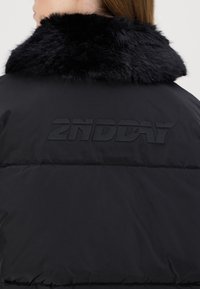 Black puffer jacket featuring a plush black faux fur collar and embossed "2NDDAY" logo on the back. Smooth texture with a soft finish.