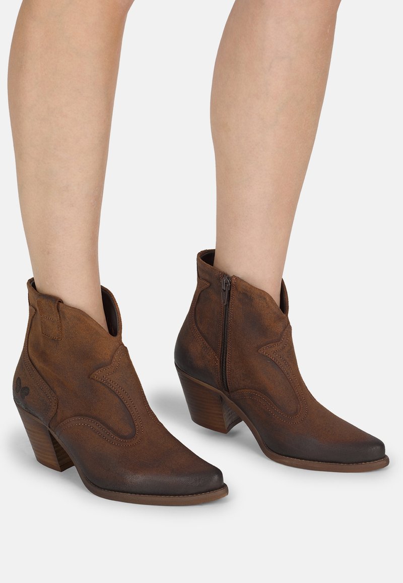 Botas de tobillo de cuero marrón con punta afilada, cremallera lateral y costuras decorativas. El tacón apilado añade altura, con un sutil logotipo.