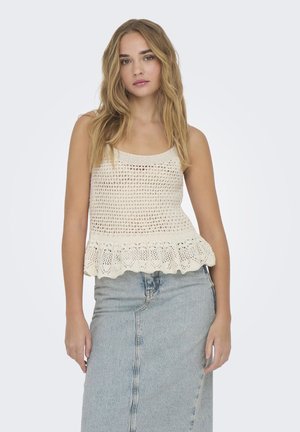 Beige virkad linne med en utställd fåll, som har ett öppet stickat mönster och vågiga kanter, ihop med en hög midja denimkjol.