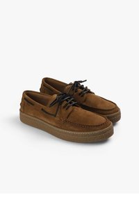 Brune ruskindsko med et lavprofildesign, sorte snørebånd og en tekstureret gummisål. Har kontrasterende syninger og sidelister.