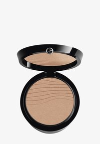 Bronzer en poudre dans un compact noir rond. Intérieur lisse et scintillant de couleur marron clair avec une texture en vagues. Présente un logo sur le couvercle.