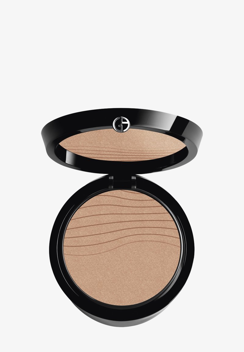Bronzer en poudre dans un compact noir rond. Intérieur lisse et scintillant de couleur marron clair avec une texture en vagues. Présente un logo sur le couvercle.
