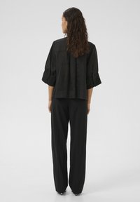 Black linen shirt with short, rolled sleeves and a relaxed fit. Paired with black wide-leg pants, creating a streamlined silhouette.