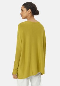 Haut ample à manches longues en tricot jaune moutarde, avec un col rond et des accents côtelés aux manches et à l'ourlet.