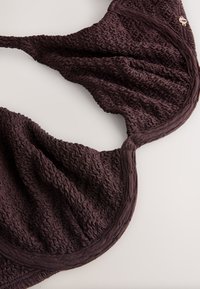 Haut de bikini en tissu texturé marron foncé avec bretelles réglables et couture sous-armature, posé à plat sur une surface claire.