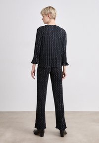 Ensemble deux pièces noir à motifs comprenant un haut ample à manches longues et un pantalon assorti avec des bas évasés et un motif à rayures verticales.
