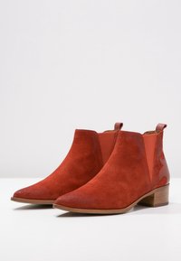 Botas de tobillo de ante rojo con punta afilada, paneles laterales elásticos y un pequeño tacón apilado. Acabado texturizado con acentos lisos.