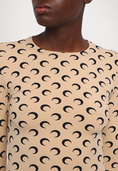 Top de manga larga en tela beige con un patrón repetido de lunas crecientes negras y un escote redondeado. Textura suave, diseño ajustado.