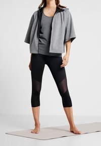 Grå croppad hoodie med dragkedja framtill, tillsammans med en grå tanktop och svarta capri leggings med genomskinliga sidopaneler.