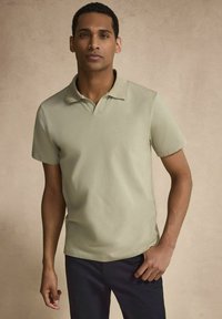 Ljusgrön pikétröja i slät väv, med krage och korta ärmar, ihop med marinblå byxor. Enkelt och figursytt design.