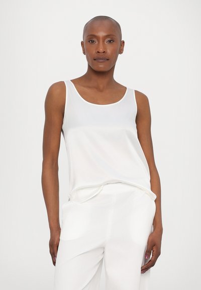 Valge ilma varrukateta särk, millel on sile tekstuur, ümmargune kaelus ja mugav lõige. Kombineeritud valgete, lõdva lõikega pükstega.