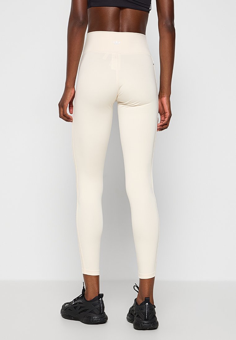 Leggings a vita alta in beige chiaro, realizzati in tessuto elasticizzato. Presentano un design elegante e una trama liscia, abbinati a scarpe da ginnastica nere.