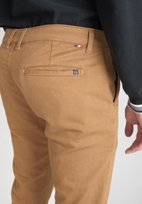 Khaki byxor med en jämn textur; bältesöglor och fickor; har en liten logotyp med blå, vit och röd färgaccent nära midjebandet.