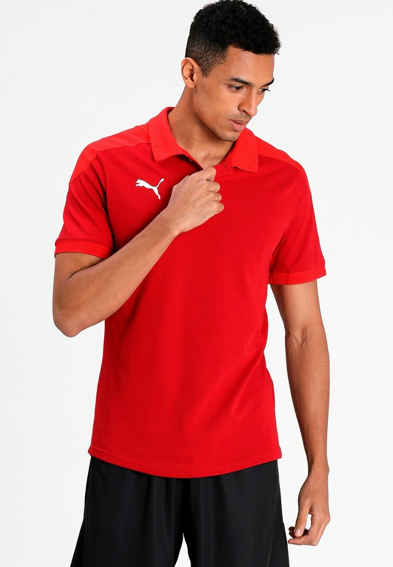 Rød polo skjorte med korte ærmer, krave og hvidt Puma-logo. Glat stof med tætsiddende design, parret med sorte shorts.