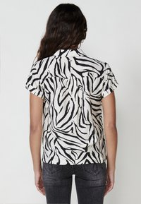 Camisa de manga corta con un diseño de estampado de cebra, con rayas negras sobre un fondo blanco, con un cuello clásico y un ligero brillo.