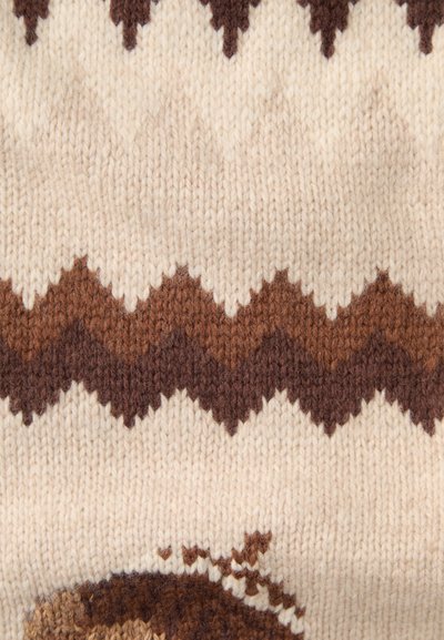 Nærbillede af beige strikket stof med brune zigzag-mønstre og strukturerede uldfibre.
