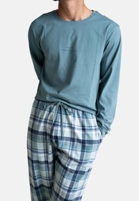 Lange mouw teal katoenen shirt met een centraal logo; gecombineerd met lichte geruite pyjamabroek in lichtblauw, donkerblauw en witte tinten.