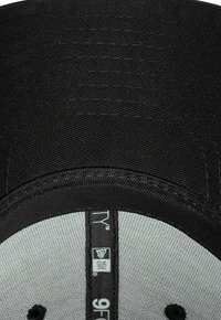 Schwarze Stoffkappe mit flachem Schirm, grauer Unterseite und abgesteppten Details. Enthält ein Etikett mit Marken- und Größenangaben.