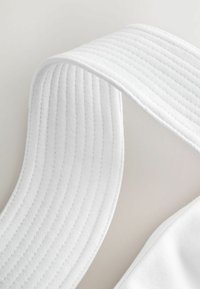 Vit tygband med ribbad textur, med en släta kant och en vikt hörn för extra detalj. Mjuk och flexibel design.