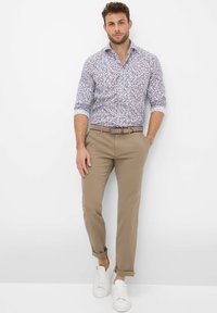 Hemd mit Knopfleiste, weißer Grundfarbe und blauem Blumenmuster, kombiniert mit khakifarbenen Chinos und weißen Turnschuhen, mit hochgekrempelten Ärmeln und einem Gürtel.