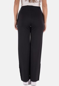 Pantaloni neri a gamba larga con cintura elastica, caratterizzati da spacchi laterali e un tessuto morbido e elasticizzato. Abbinati a sneakers bianche.
