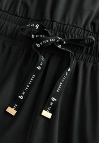 Zwarte stoffen shorts met een elastische tailleband, voorzien van een trekkoord van gemerkte zwart-witte ribbon met gouden hardware accenten.