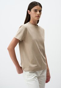 T-shirt beige a maniche corte realizzato in tessuto morbido, caratterizzato da un classico collo rotondo e una linea diritta con cuciture minime per un aspetto elegante.