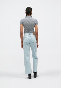 Svetlo modre kavbojke širokih hlačnic z visokim pasom, kombinirane z sivi kratkimi rokavi s karo vzorcem in detajlom vezave na hrbtu. Črni gležnarji.