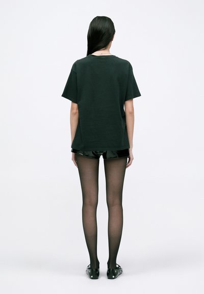 Tricou negru cu mânecă scurtă, cu o croială lejeră, asociat cu pantaloni scurți negri lucioși, ciorapi negri translucizi și pantofi negri. Design minimalist, fără modele.
