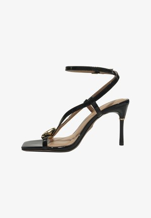 Sandalia de tacón alto de charol negro con tira en el tobillo, punta cuadrada y detalle de hebilla dorada en la tira frontal.