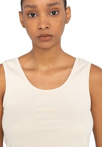 Lys beige ribbet tanktop med rund hals og minimal branding. Stoffet har en glat overflade og subtile designdetaljer.