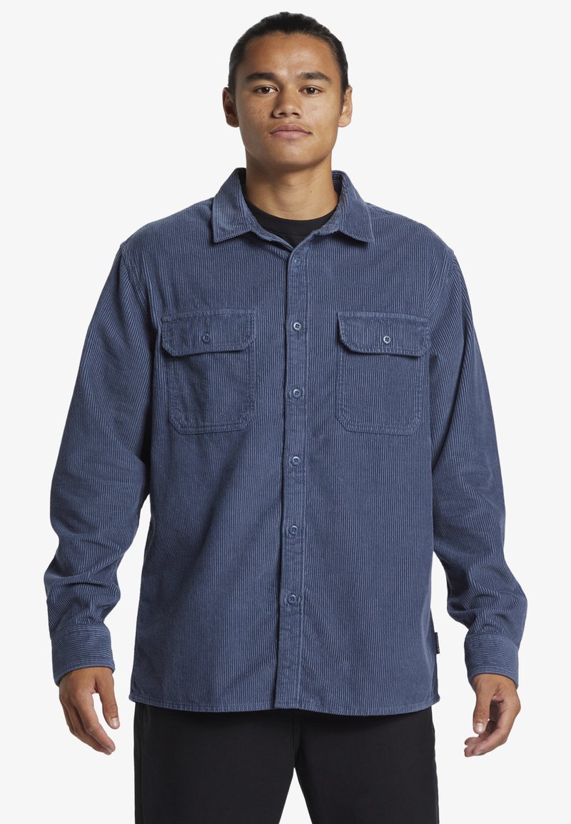 Camisa de pana en color azul marino con cierre de botones en la parte delantera, dos bolsillos en el pecho y cuello. Presenta una tela texturizada y un corte relajado.